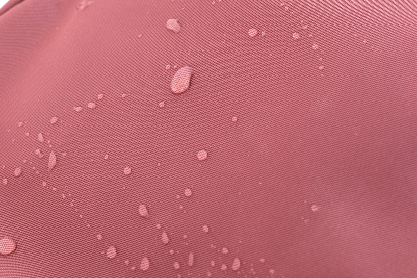 Close-up of a pink fabric with water droplets, possibly demonstrating water resistance.